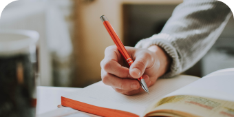 Person holding a pen and writing on a notebook.